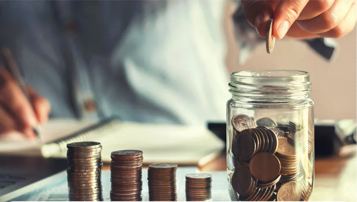 Monedas apiladas y un frasco de ahorro